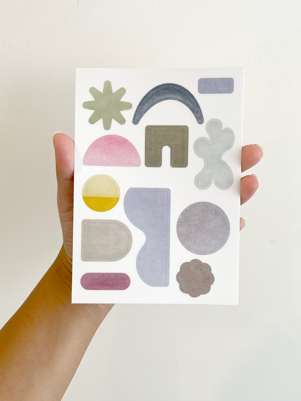Hand holding a sheet of colorful geometric stickers against a white background