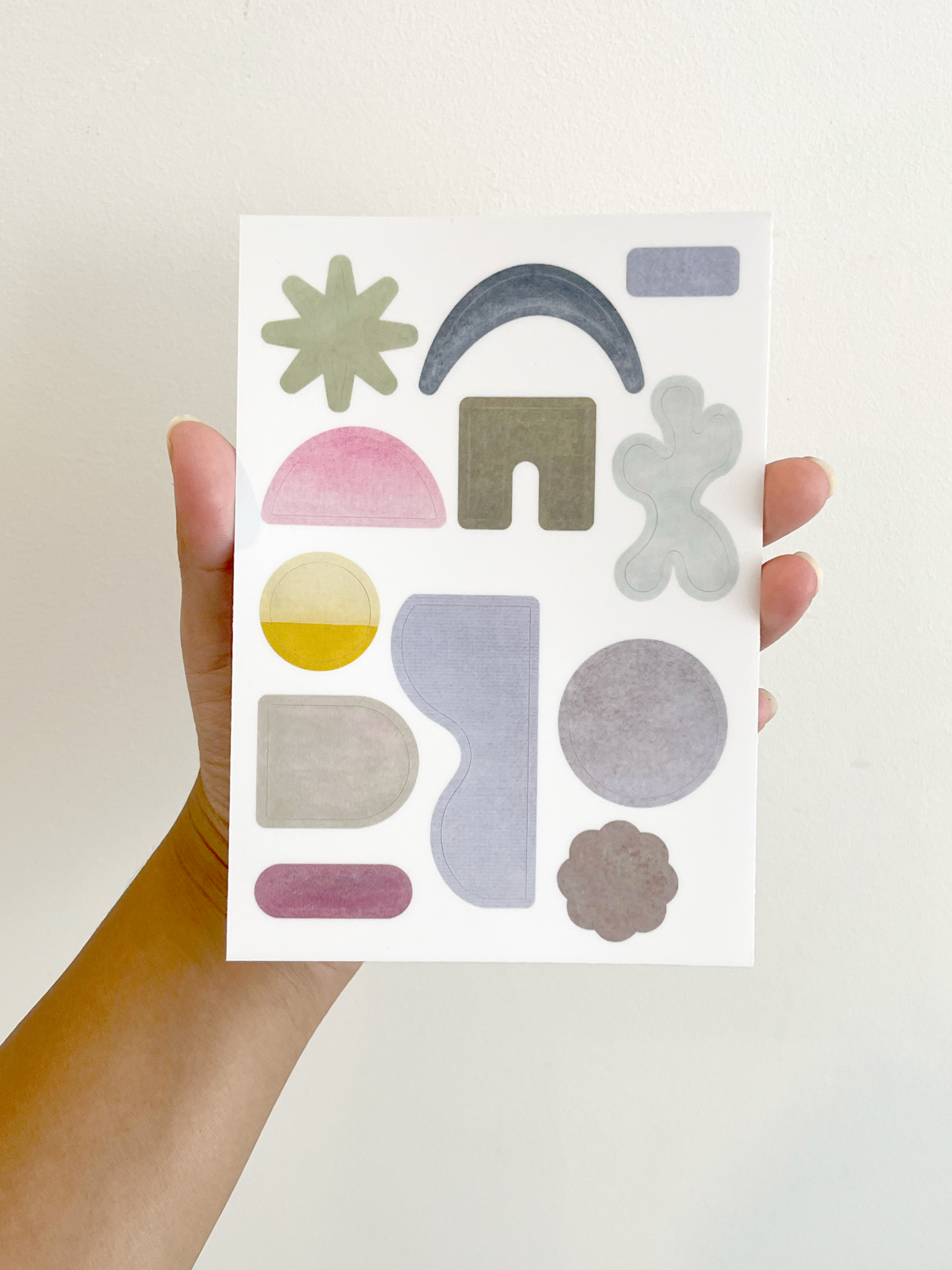 Hand holding a sheet of colorful geometric stickers against a white background