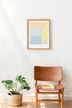 Wooden chair with a plant and book next to a framed abstract art piece on a white wall.