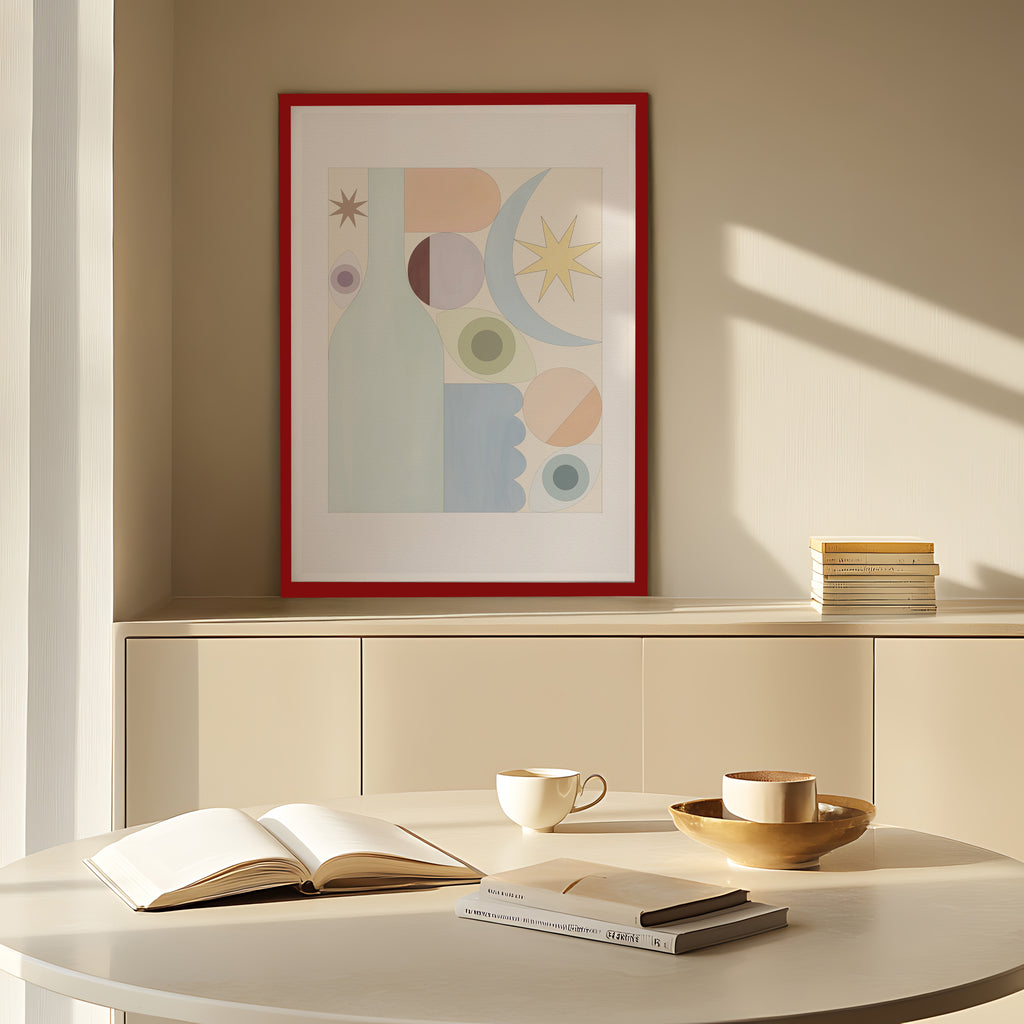 Abstract framed artwork on a wall with a table featuring books and a cup.