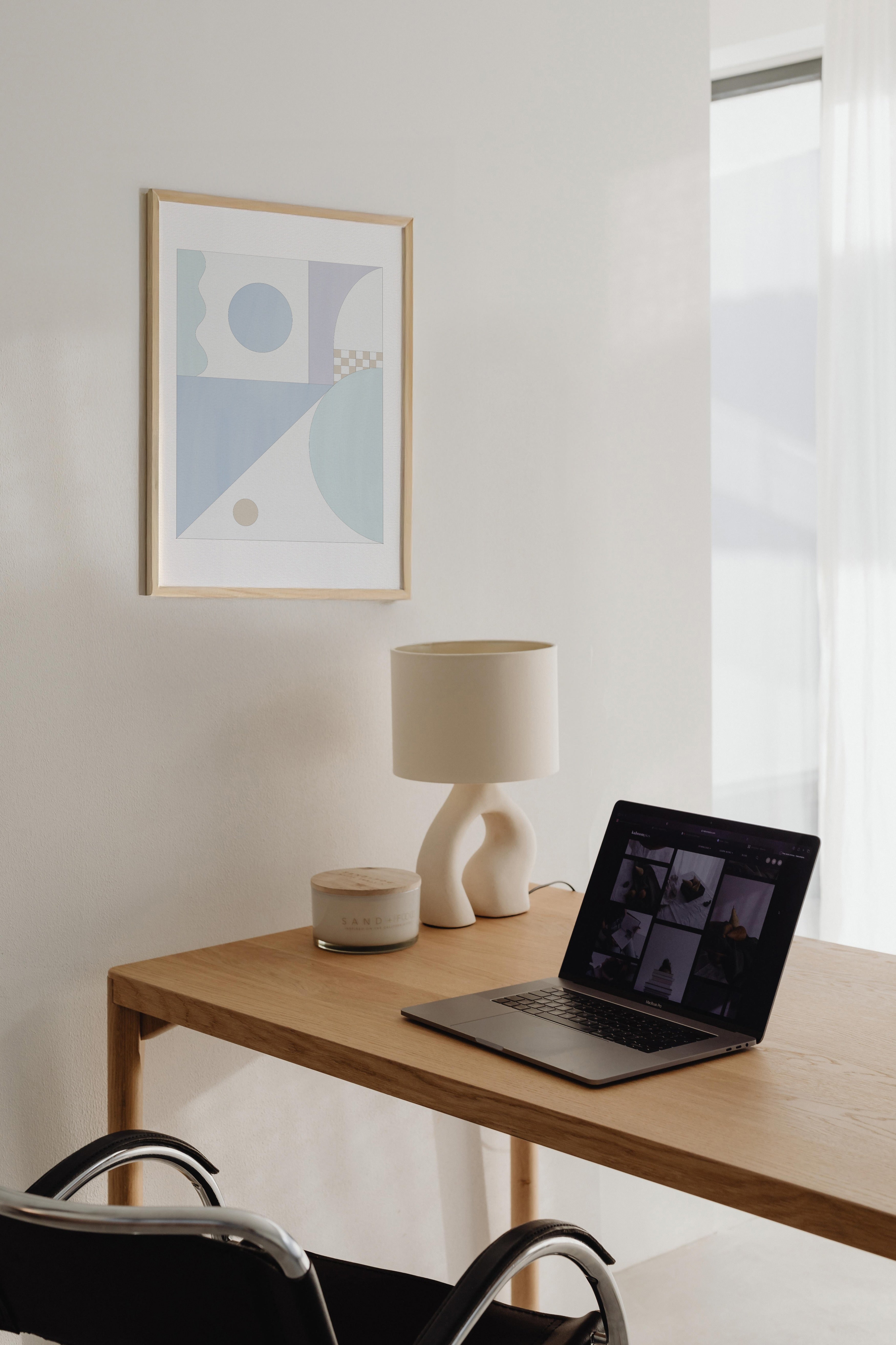 Modern home office with a wooden desk, laptop, lamp, and abstract art on the wall.