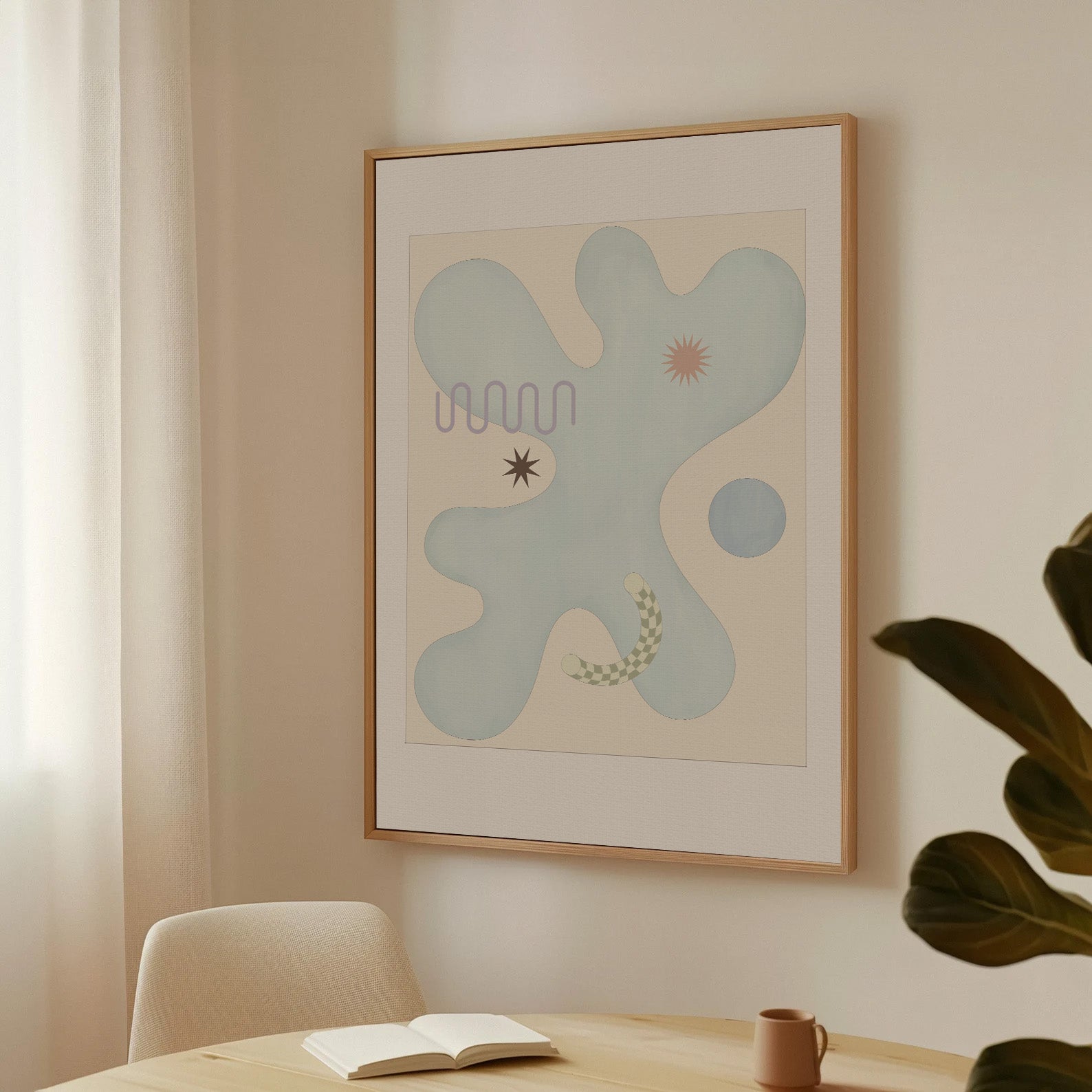 Framed abstract artwork on a wall above a table with a book and mug.