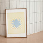 Framed artwork with a blue star design on a beige background against a tiled wall.