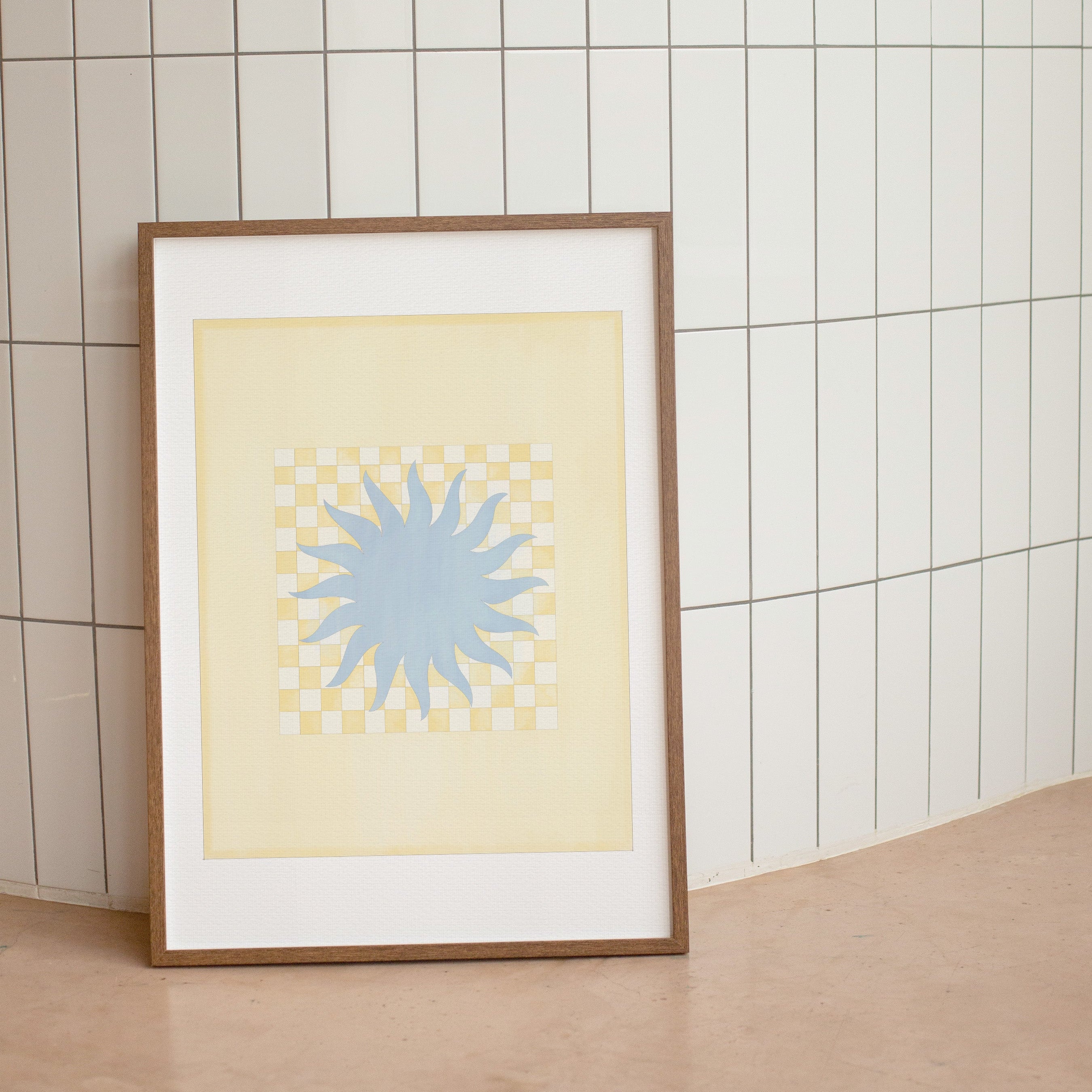 Framed artwork with a blue star design on a beige background against a tiled wall.